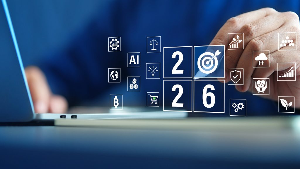 Person using a laptop with a blue background, surrounded by floating digital icons showing “2026” and symbols for AI, finance, sustainability, shopping cart, target, blockchain, and other business and technology goals.